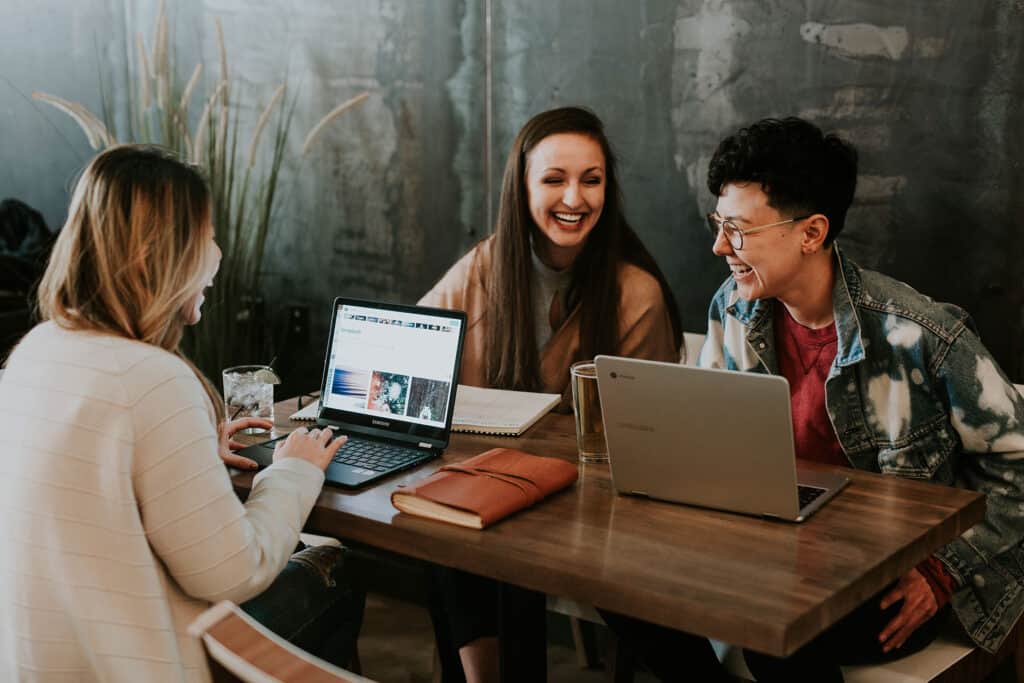 Group of teens laughing and working on laptops at a shared table