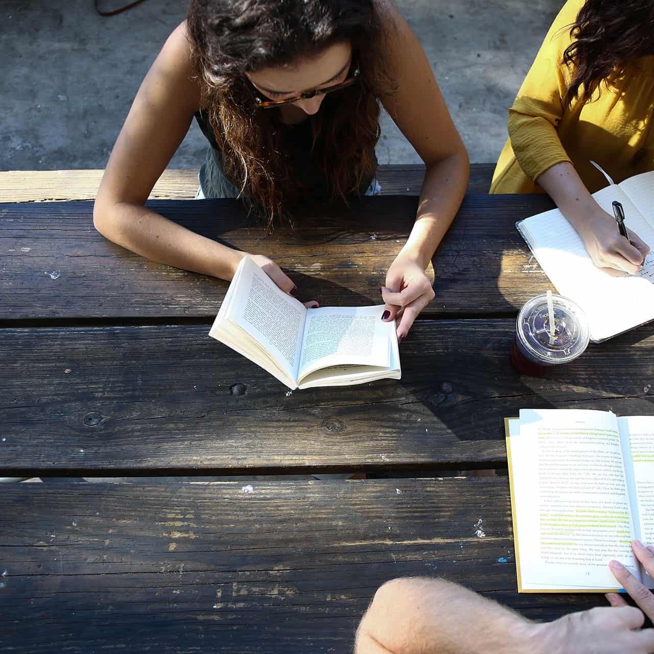 A group of friends reading and studying together outdoors at a picnic table